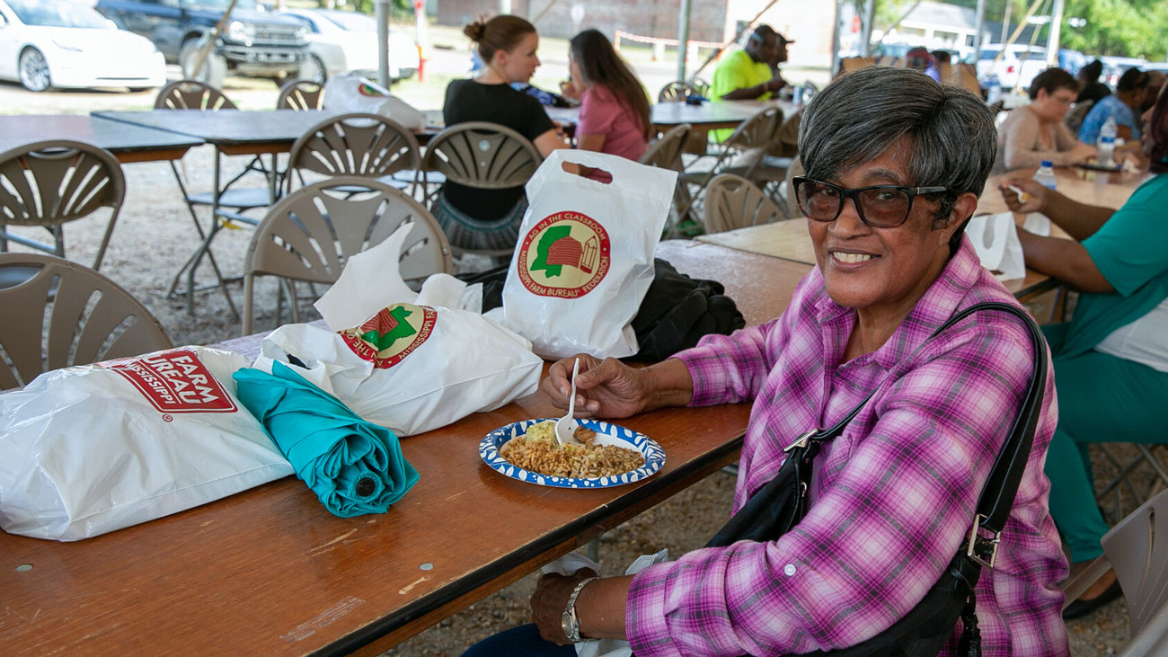A woman with sunglasses sitting at a picnic table with a plate. 