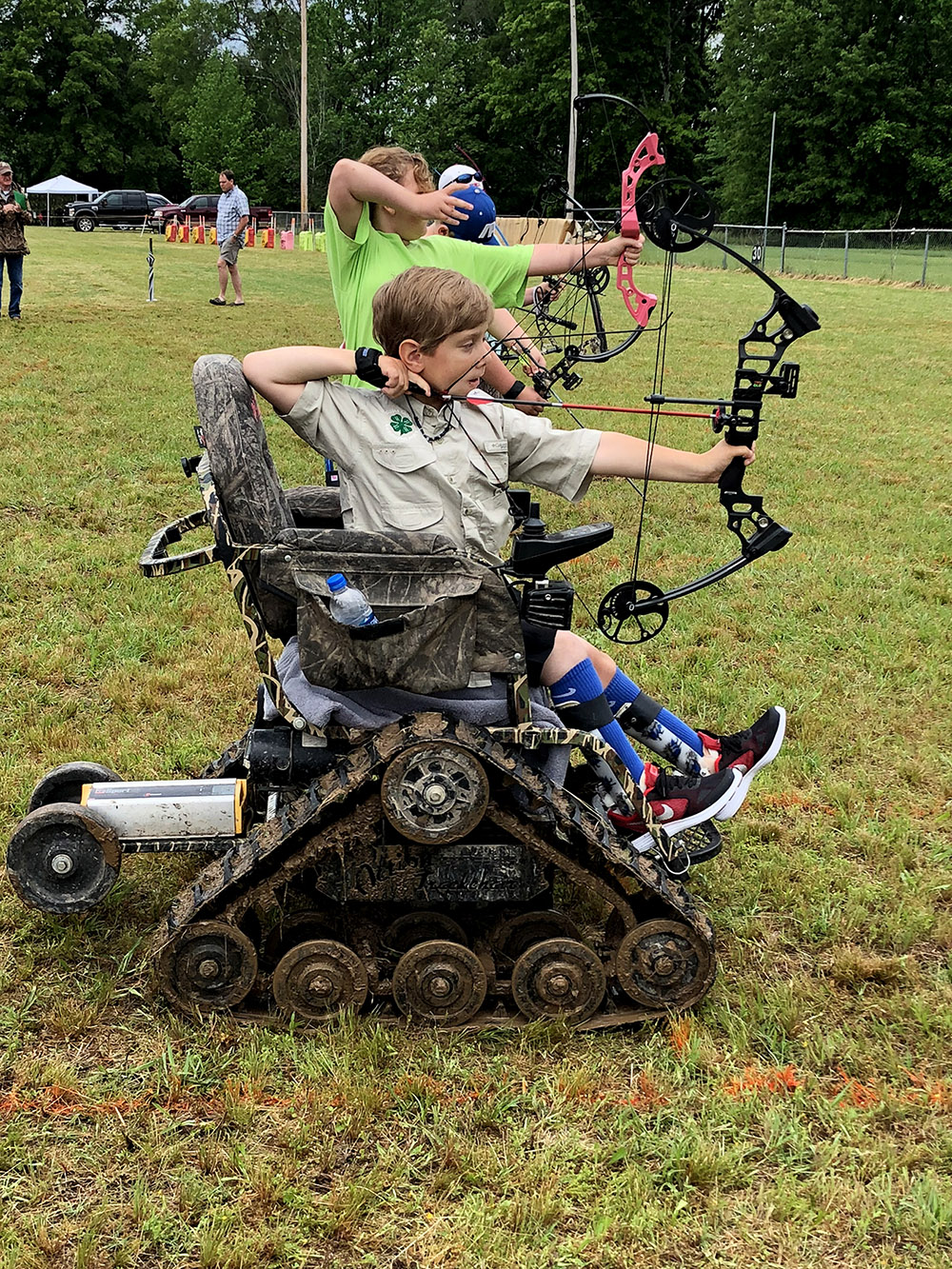 A shooting sport participant aims his bow and arrow while sitting in his specially designed wheel chair.